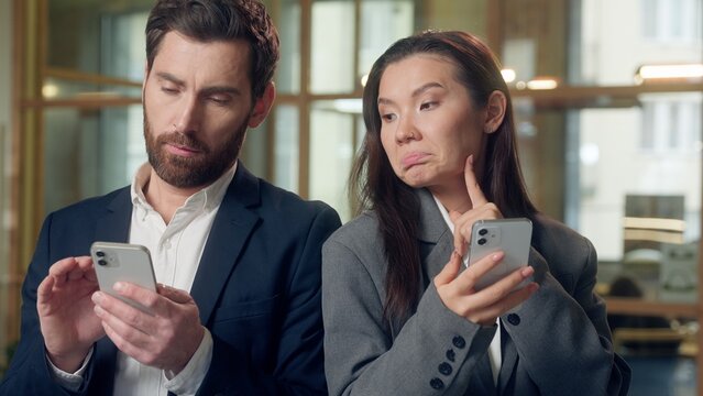 Multiethnic office business coworkers searching online smartphone internet Korean woman thoughtful scrolling mobile phone shaking finger no Caucasian man peeking screen solving issue digital research