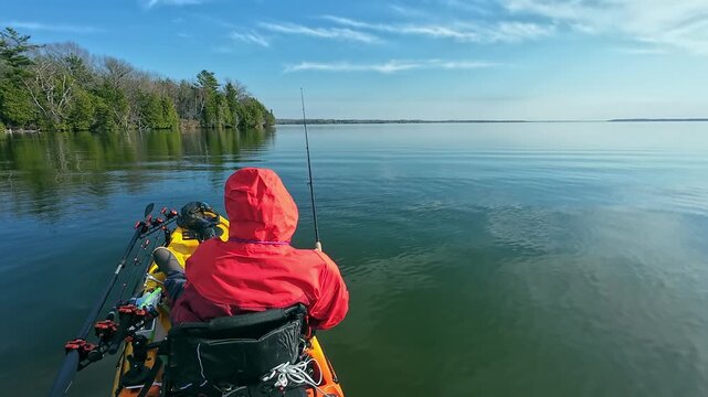 Kayak angler finesse fishing in the lake, using kayak, spinning rod and small lure. Fisherman kayaking in the North American waters, fishing and trolling fishing. Water sport in spring. Fishing game.