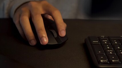 Close-up of a hand using a black computer mouse on a dark desk with a keyboard, illustrating digital work or gaming - Powered by Adobe