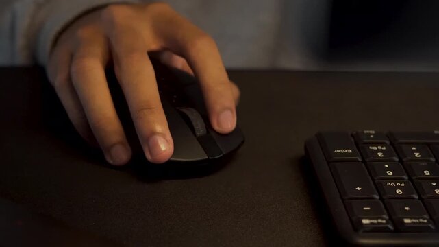 Close-up of a hand using a black computer mouse on a dark desk with a keyboard, illustrating digital work or gaming