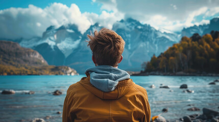 Fototapeta premium Man with his back to the camera looks at the mountain lake view, enjoying the peaceful scenery.