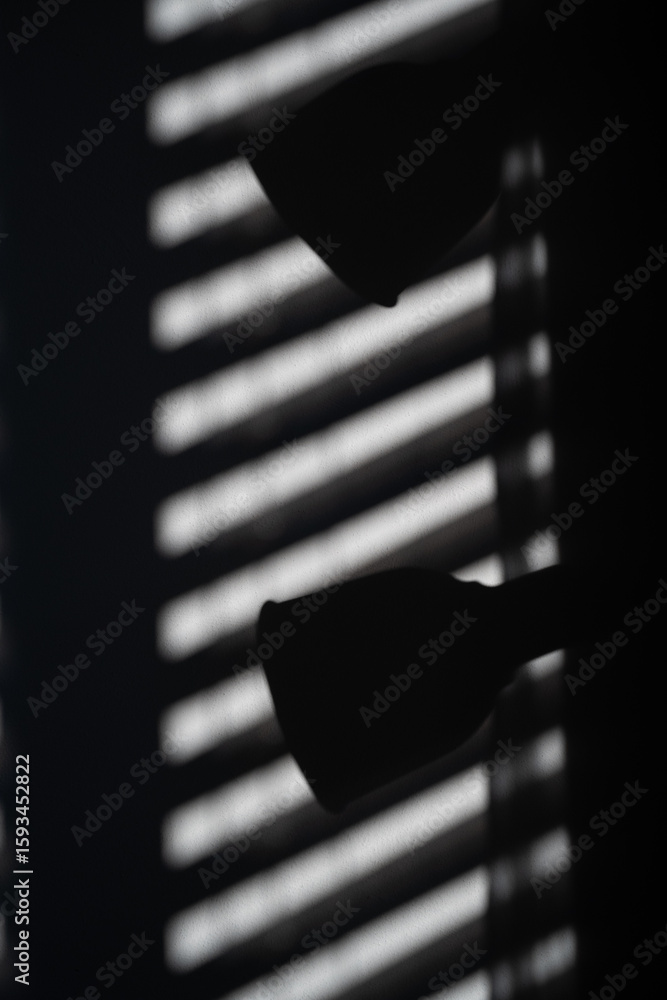 Poster a window with a blinds that is partially open, casting a shadow on the wall. the shadow is long and 