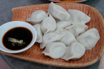 A serving of steamed dumplings arranged on a woven, rectangular bamboo steamer basket