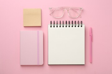 Notebooks, sticky notes, glasses and pen on pink background, flat lay