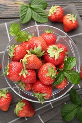 Fresh ripe strawberries and leaves in container on black wooden table, flat lay