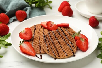 Tasty Dutch waffles (stroopwafels) with strawberries, mint and chocolate sauce on white marble table, closeup