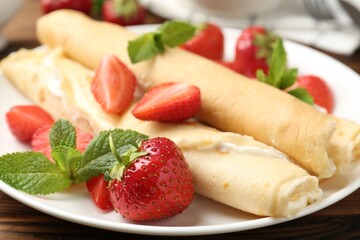 Tasty crepes with cream, strawberries and mint on table, closeup