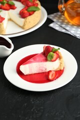 Piece of tasty cheesecake with strawberries, sauce and mint on black table, closeup