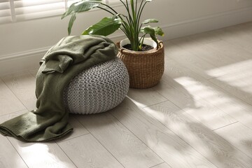 Stylish knitted pouf with plaid and houseplant at home