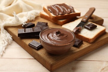 Tasty chocolate butter in bowl, pieces and sandwiches on wooden table, closeup