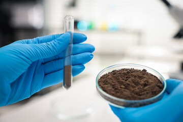 Scientist holding Petri dish with soil sample and test tube in laboratory, closeup