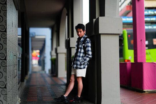 The image shows a young man leaning against a pillar in a covered walkway or arcade