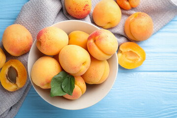 Fresh apricots with green leaves on light blue wooden table, flat lay