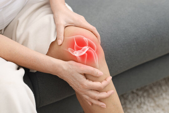 Arthritis. Woman suffering from pain in her knee on sofa, closeup. Illustration of joint inflammation on his leg