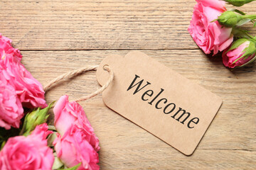 Welcome card and roses on wooden background, top view