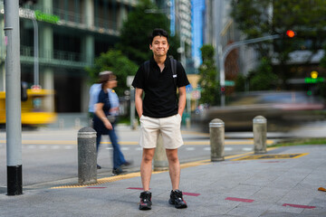 young man standing on a street corner in an urban area. He is wearing a black shirt, light-colored...