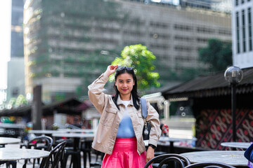 Fototapeta premium The image shows a young woman posing for a photo outdoors in an urban setting. She is wearing a light-colored jacket