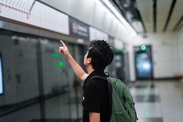 The image shows a young man, wearing a backpack, pointing at a map or information board, likely in a subway or metro station