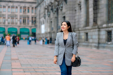 Confident young Latina business woman in gray blazer walking near MUNAL in Mexico City, smiling...