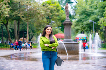 Young smiling Latina woman in green blouse and jeans walking through the Alameda Central park in...