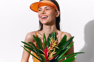 Cheerful young model holding tropical flowers, wearing an orange visor and a bright outfit, set...