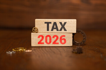 TAX 2026 word on wooden block with calculator and notebook on wood background.