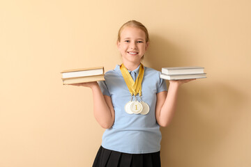 Cute little schoolgirl with medals and books on beige background