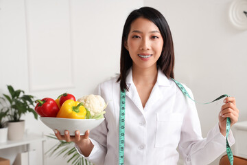 Female Asian nutritionist with healthy food and tape measure in office