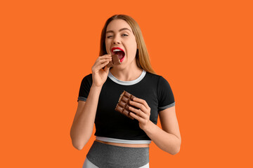 Young woman eating chocolate bar on orange background