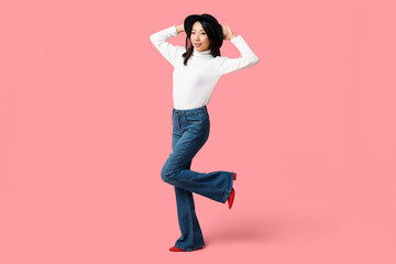Beautiful young happy Asian woman in stylish jeans on pink background