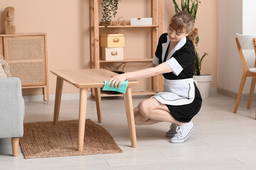Smiling maid cleaning wooden table in living room