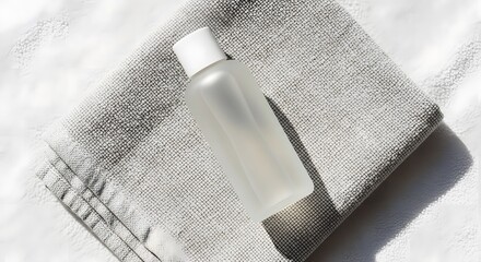 A small, transparent bottle rests on a folded, grey towel, bathed in sunlight.
