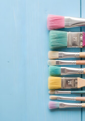 Fototapeta premium A collection of paintbrushes with various bristle colors arranged neatly on a light blue wooden surface.