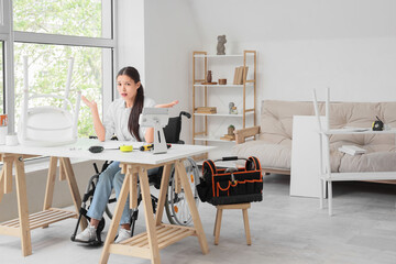 Upset young Asian woman in wheelchair assembling chair at home