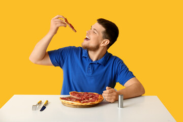 Young man with tasty pepperoni pizza at table on yellow background