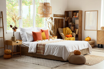 Interior of cozy bedroom with bed, armchair, pillows and pumpkins