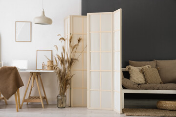 Interior of stylish room with brown sofa, folding screen and workplace