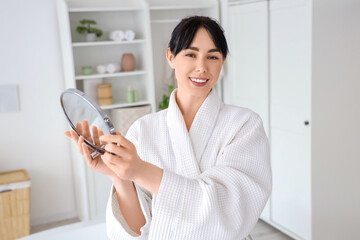 Young woman in waffle robe with mirror at home