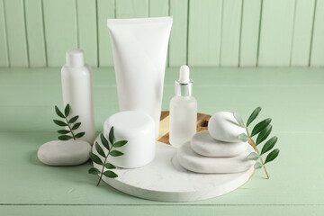 Composition with spa stones, green leaves, jar and bottles of cosmetic products on green wooden background, closeup