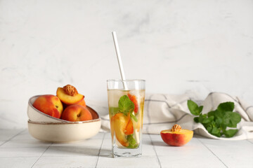 Glass of fresh peach lemonade with mint and fruits on white tile table