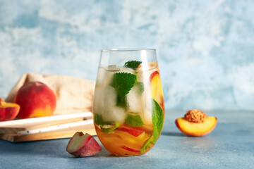 Glass of fresh peach lemonade with mint on blue background