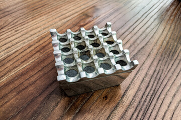 square metal ashtray with multiple indentations sits on a wooden table, showcasing a practical yet decorative item.