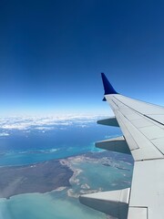 Stunning aerial view from airplane window showing tropical coastline with turquoise waters, small...