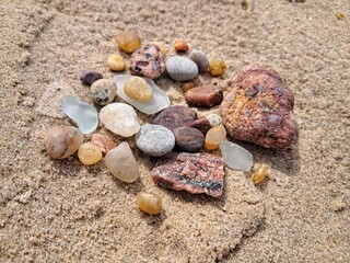 A diverse assortment of smooth and textured beach stones, collected from the shore, lies in a...
