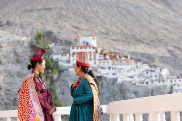 Two women in traditional attire converse joyfully on a balcony overlooking Hunder Monastery in Leh,...