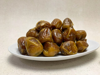 A white plate brimming with glossy, brown Sukkari dates (sukari dates). Delicious and sweet natural fruit.
