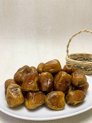 A plate of glossy Sukkari dates (sukari dates), with a small woven basket in the background. Sweet, natural fruit.