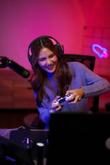 Asian young adult female streamer enjoys intense video game play live broadcasting from home gaming...