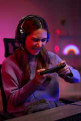 Young Asian woman intensely playing mobile game wearing headphones gaming room dark neon light