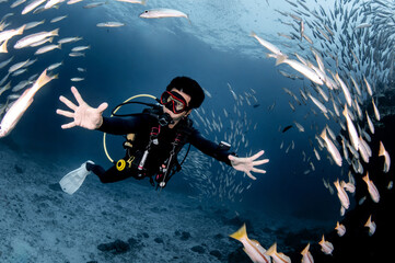 Male scuba diver diving with a school of snapper fish at Racha Island, a popular dive site in Phuket, Thailand. Underwater world experience in Andaman sea.
